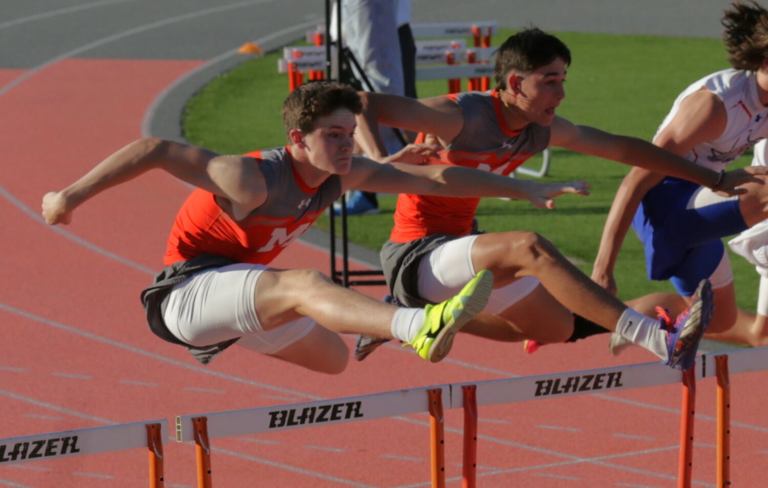 Mineola’s Chance Williams (left) and Caden Rupert are mirrored going over the second set of hurdles in the 110-meter high hurdles event. They finished second and third respectively. The event was won by Quitman’s Bryson Hobbs in 16.313. [see more speed and strength on display]